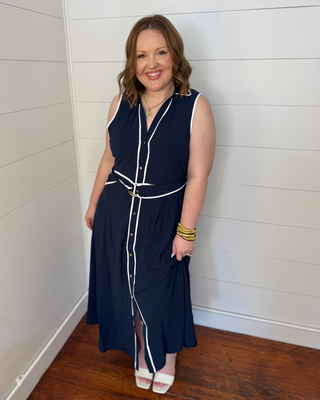 Woman wearing a navy dress with white accents against a white wall.