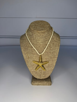 Gold starfish pendant on a rope necklace displayed on a textured mannequin bust against a plain background.
