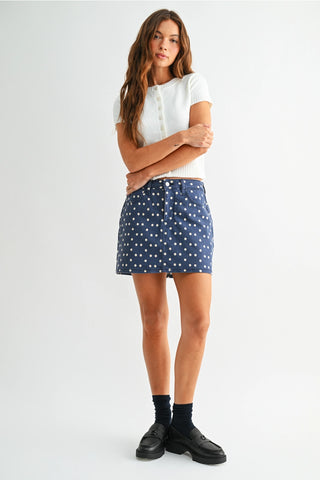 Woman in Polka Dot Denim Skort, where playful meets practical. This blue denim skort features an allover cream polka dot print, classic five-pocket styling, and a comfortable stretch fit.