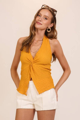 Woman wearing a mustard yellow top and white shorts on a beige background