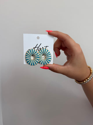 Hand holding a card with blue and gold earrings on a plain background