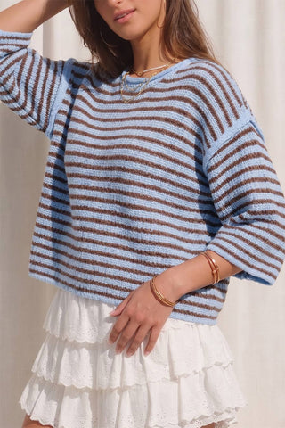 Woman wearing a blue and brown striped sweater with a white skirt against a neutral background