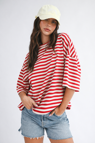 Person wearing a red and white striped shirt with denim shorts on a plain background