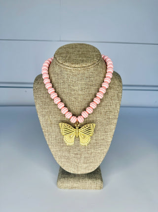 Necklace with pink beads and a gold butterfly pendant on a beige bust against a light blue background