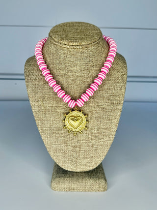 Necklace with pink beads and gold heart pendant on a brown mannequin bust against a blue background
