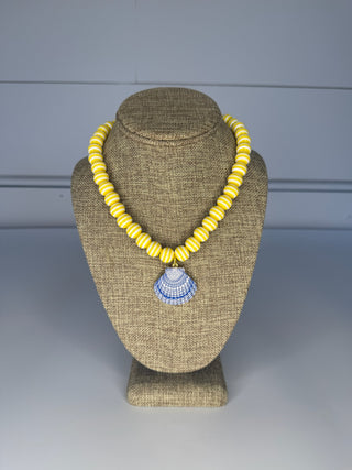 Yellow beaded necklace with a blue pendant on a brown mannequin bust against a gray background