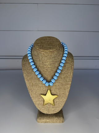 Necklace with blue and white striped beads and a gold star pendant on a brown bust against a gray background.