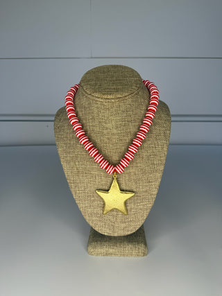 Necklace with red and white striped beads and a gold star pendant on a beige bust against a gray background.