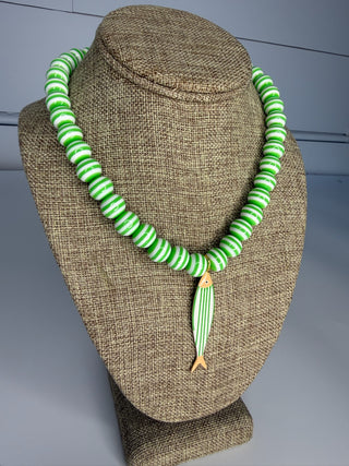 Green and white striped necklace with a fish pendant on a brown textured stand.