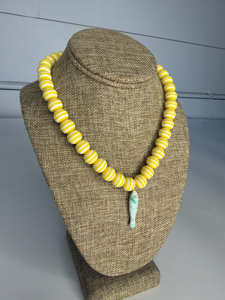 Yellow beaded necklace with a green pendant on a mannequin bust against a gray background