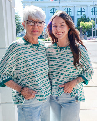 Two women wearing matching green and white striped shirts standing outdoors.