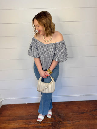 Woman in a checked off the shoulder top next to a white wall