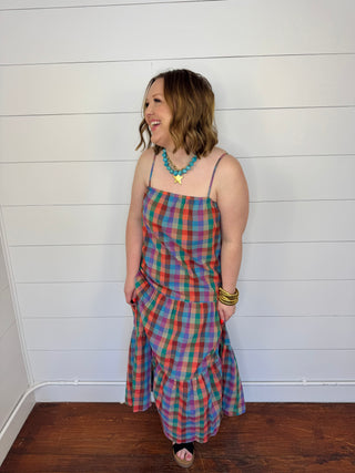 Woman wearing a colorful plaid dress standing against a white wall.