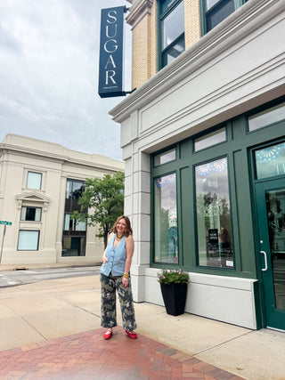 Woman standing in front of a building with a 'SUGAR' sign on a city street.