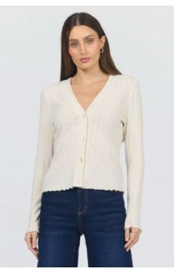 A woman modeling a cream-colored, long-sleeve button-up cardigan with a scalloped hem and ribbed texture, paired with dark blue jeans against a plain light gray background.