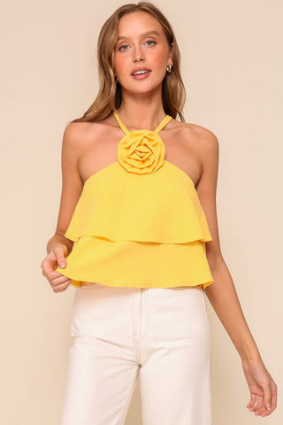Woman wearing a yellow tiered top with a floral detail on a beige background