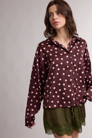 Woman wearing a brown shirt with pink polka dots and green shorts on a plain background