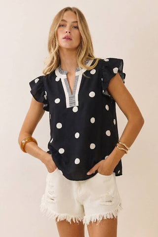 Woman wearing a black polka dot blouse and white shorts against a plain background
