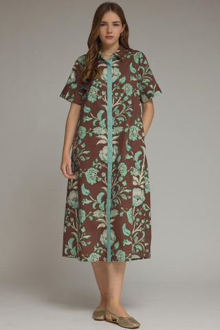 Woman wearing a brown dress with green floral pattern on a plain background
