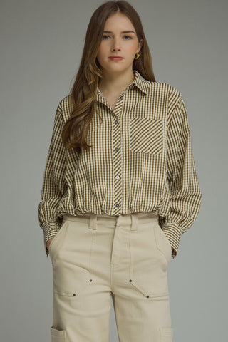 A woman modeling a beige and brown gingham long-sleeve button-up shirt tucked into cream cargo pants, set against a solid gray studio background.
