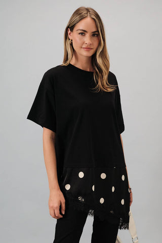 Woman wearing a black oversized t-shirt with white polka dots on a plain background