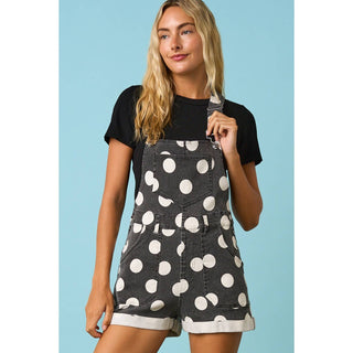 Woman wearing a black denim pinafore with white polka dots against a blue background